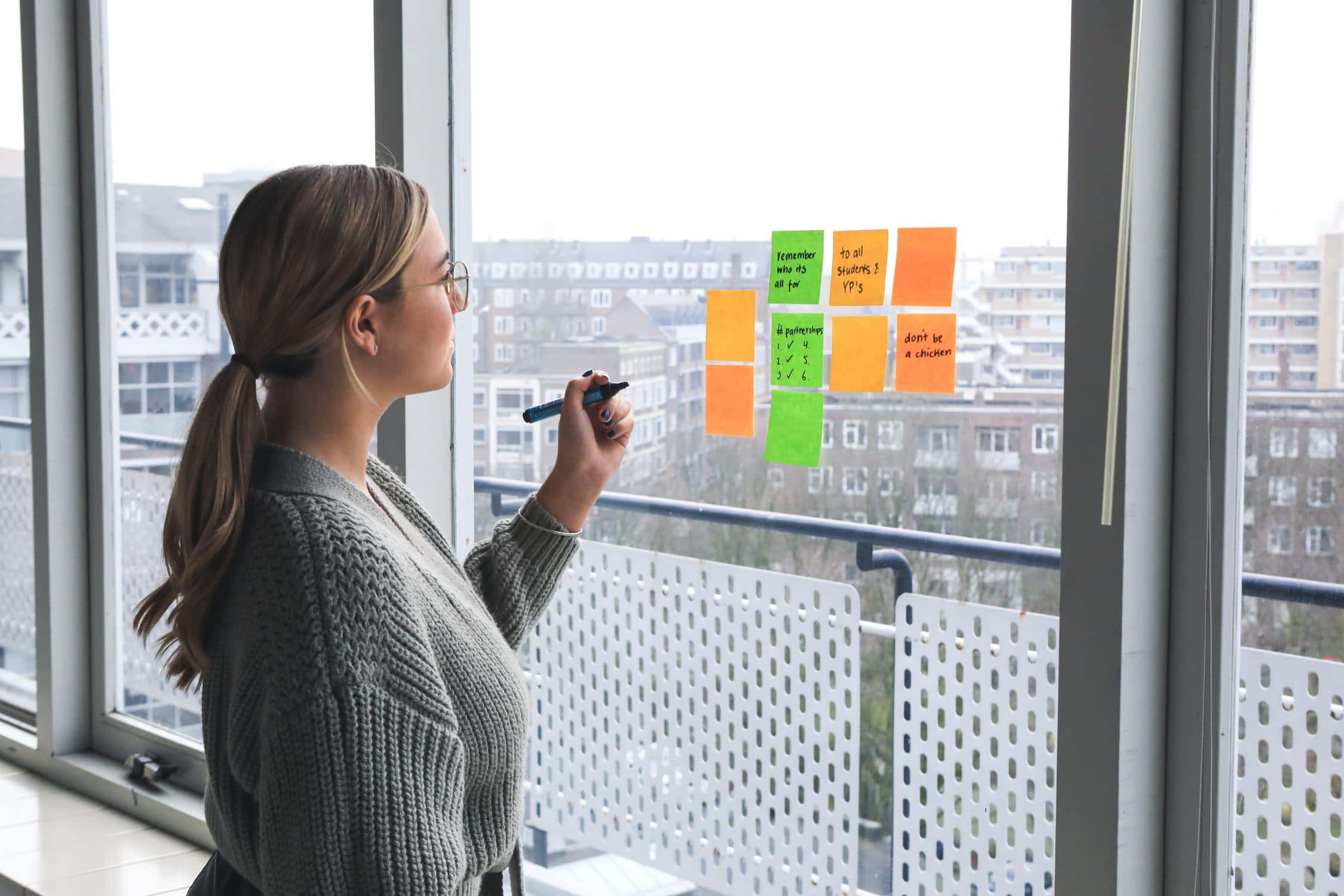 Junge Frau steht vor Fenster, an dem Post-its kleben