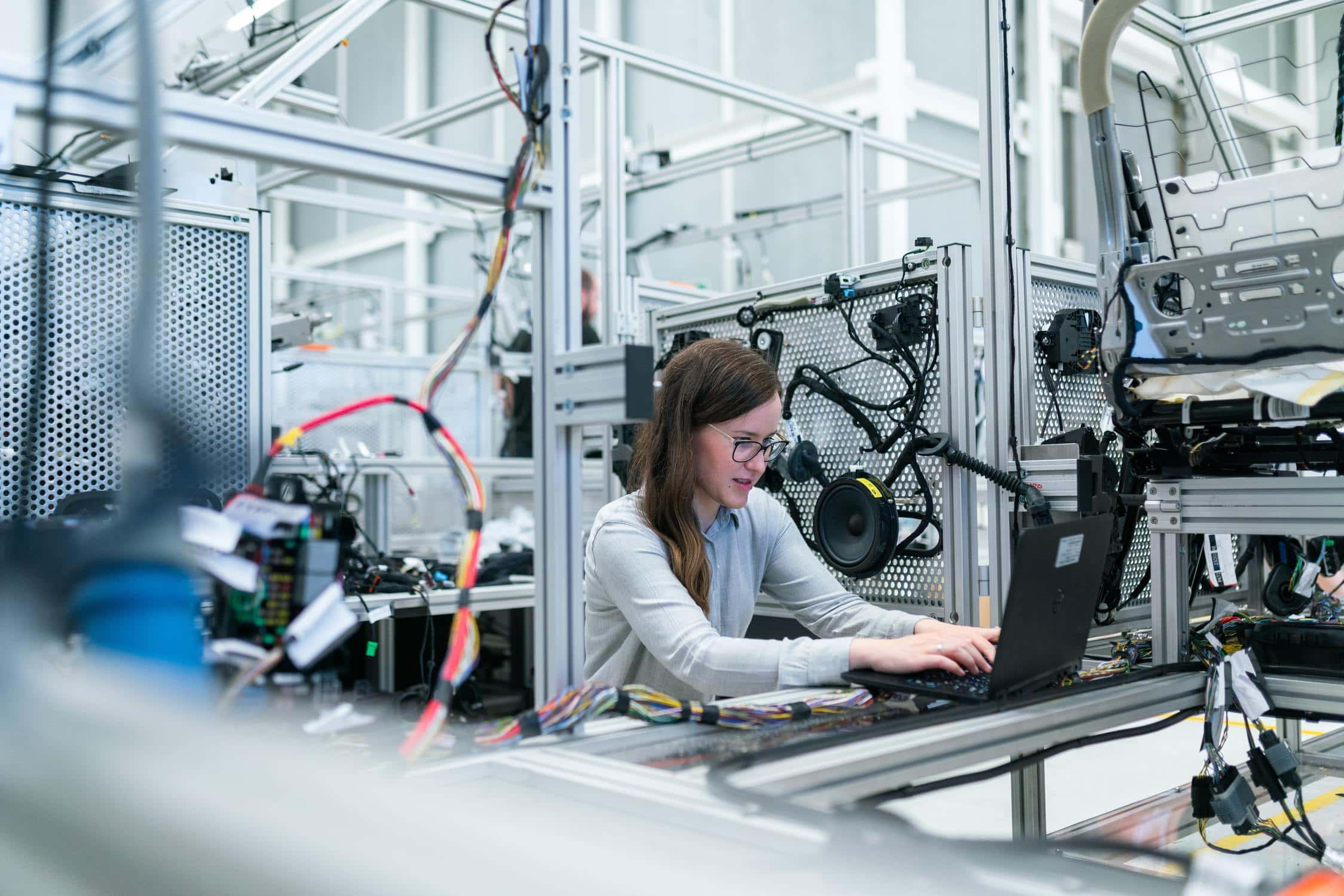 Junge Frau sitzt in großem Technik-Labor vor Computer und arbeitet an ihrer Forschung