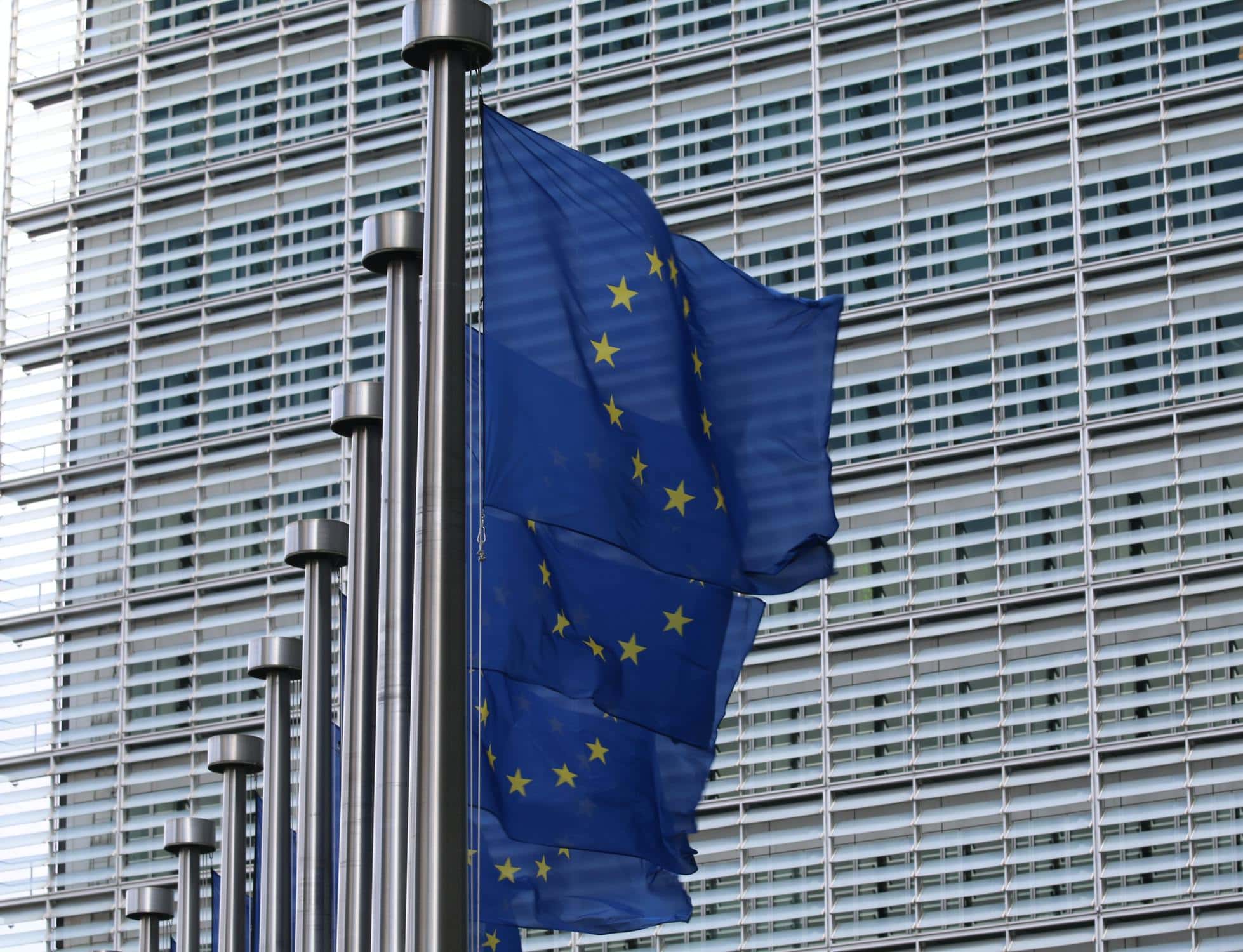 Mehrere EU-Flaggen hintereinander vor eine großem Glasgebäude