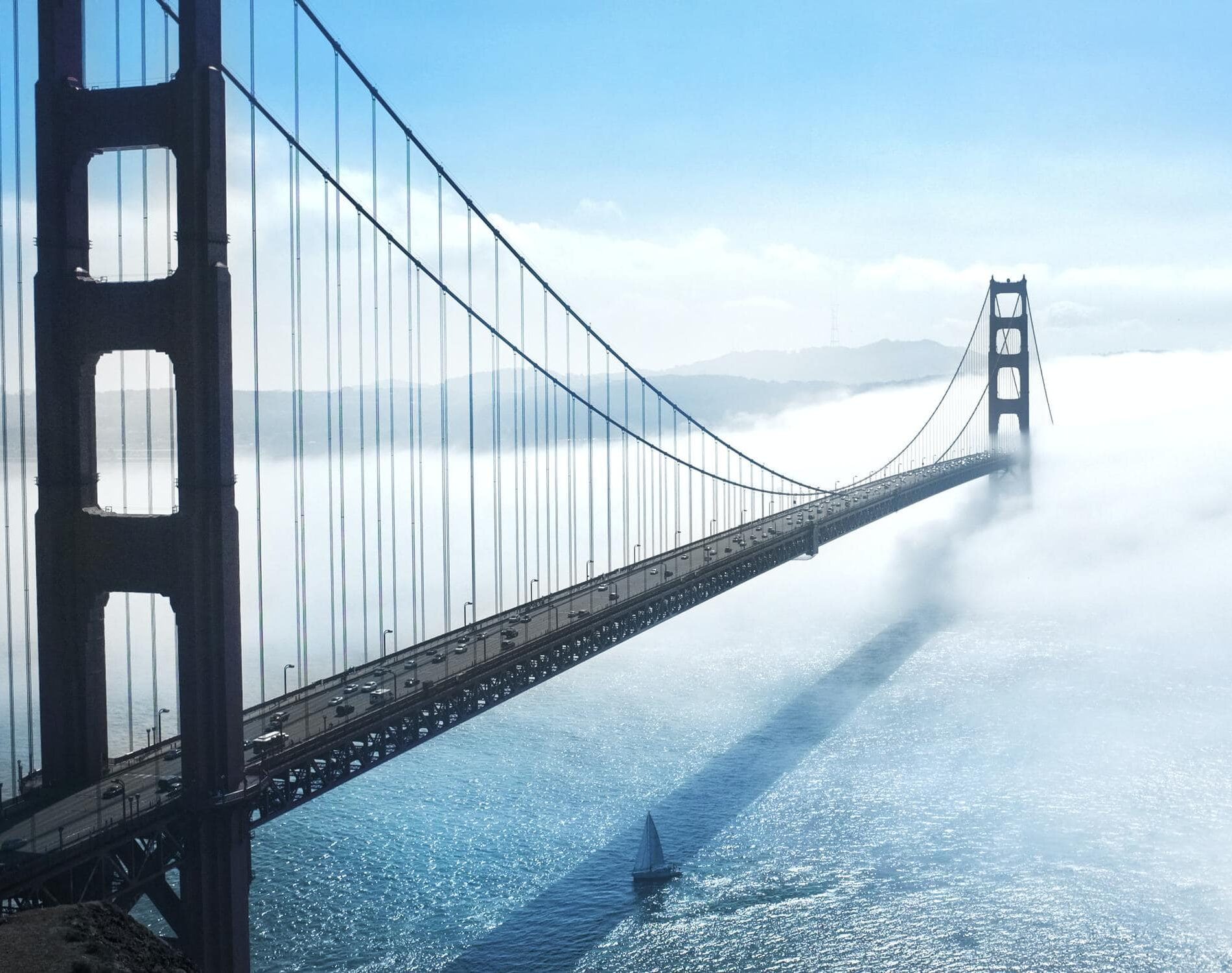 Hängebrücke über einem großen Gewässer, worüber Nebel hängt