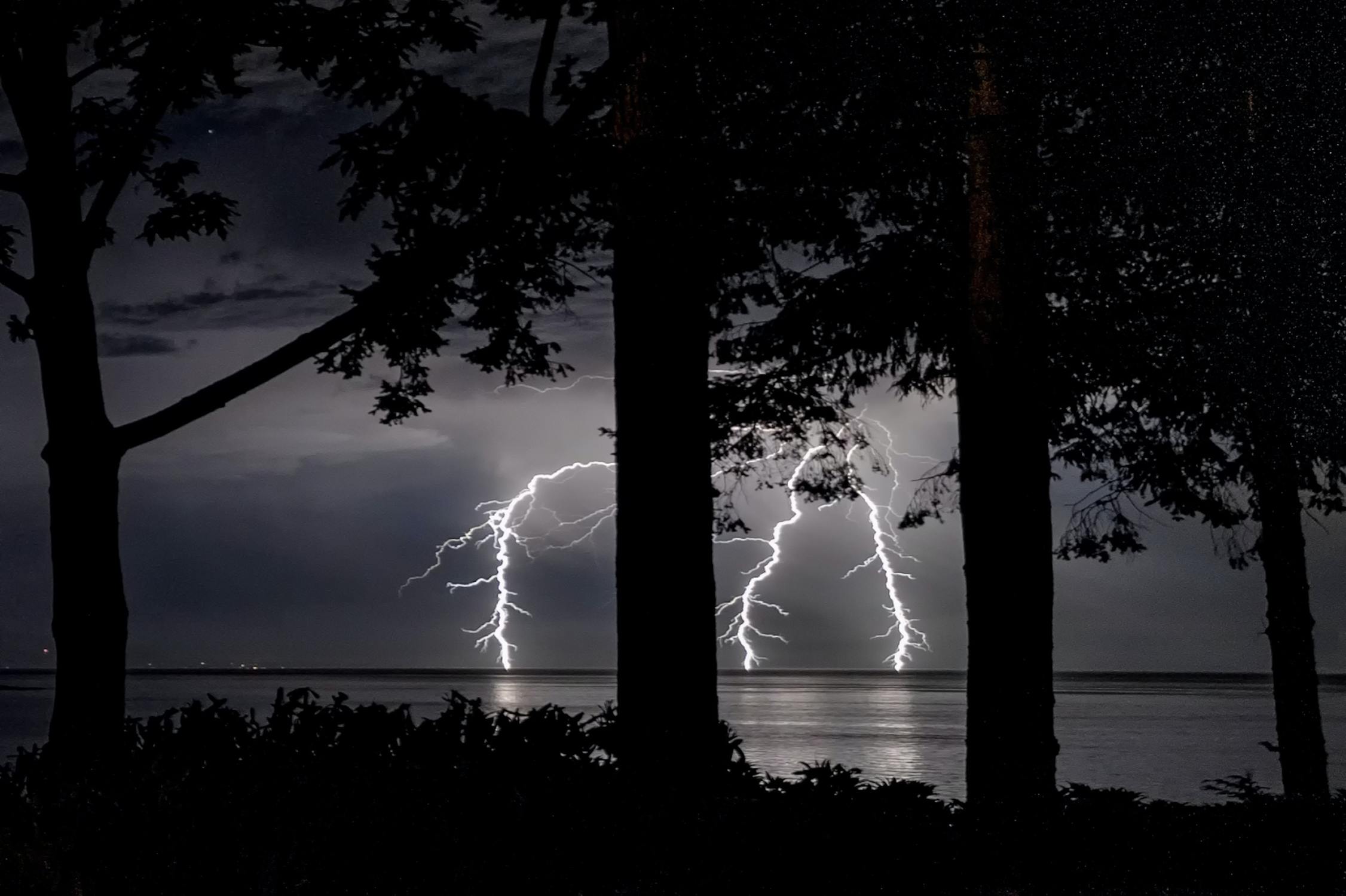 Ein Gewitter am See wird vom Wald aus beobachtet