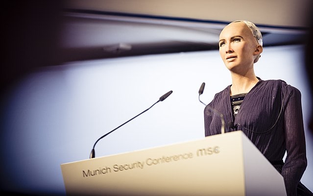 Der androide Roboter "Sophia" steht hinter einem Rednerpult mit zwei Mikrofonen.