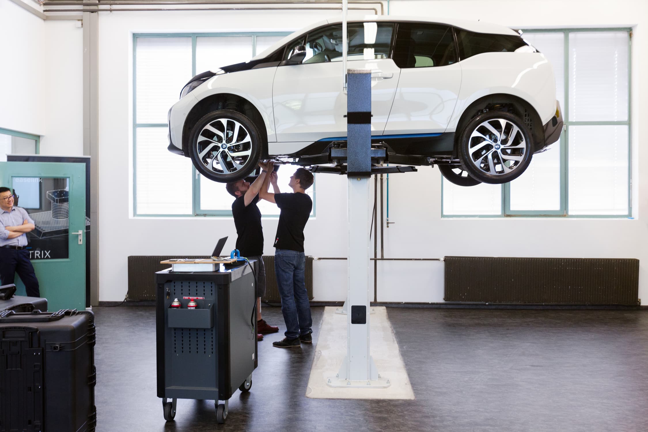 Elektro-Auto, dass auf einer Hebebühne steht. Zwei Mechaniker begutachten die Unterseite des Autos.