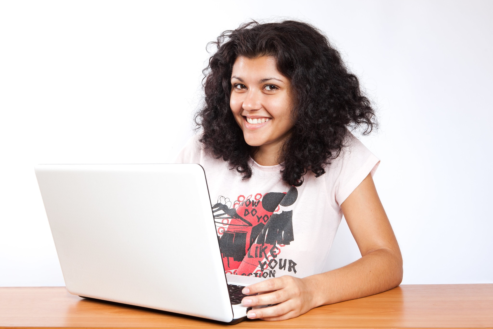 Mädchen sitzt vor Laptop und lächelt in die Kamera.