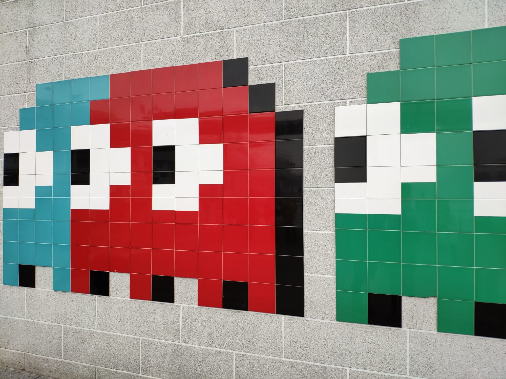Geister vom Spiel Pacman, auf Fliesenwand. Sie sind blau, grün und rot.