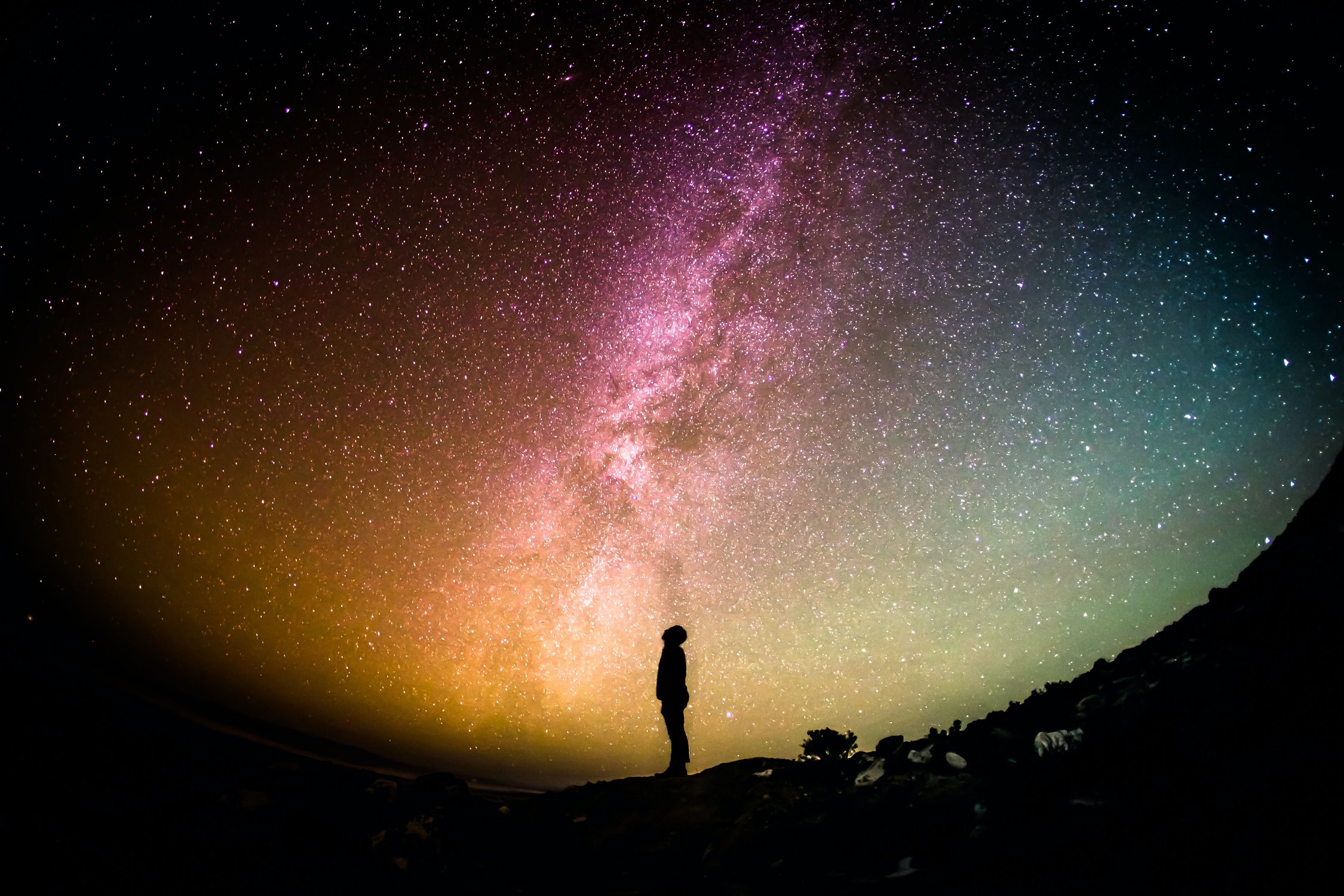 Eine menschliche Schatten-Silhouette steht unter einem Nachthimmel voller Sterne und schaut staunend nach oben.