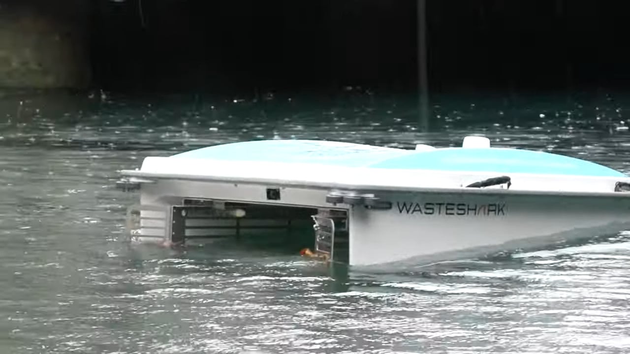 Roboterboot in Gewässer. Es hat in der Mitte einen offenen Bereich, mit dem es Müll aus dem Fluss sammelt.
