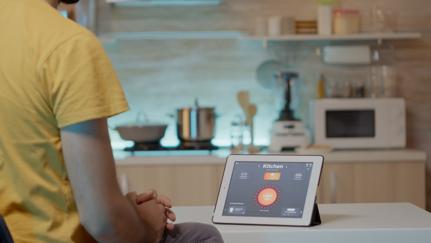 Ein junger Mann schaut auf ein mit intelligenter Software ausgestattetes Tablet auf der Küchentheke, um das Licht im Smart Home damit zu kontrollieren
