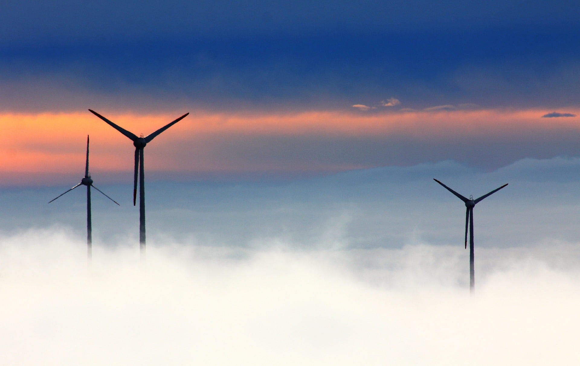 Drei Windräder vor Sonnenuntergang. Nebel steigt auf.