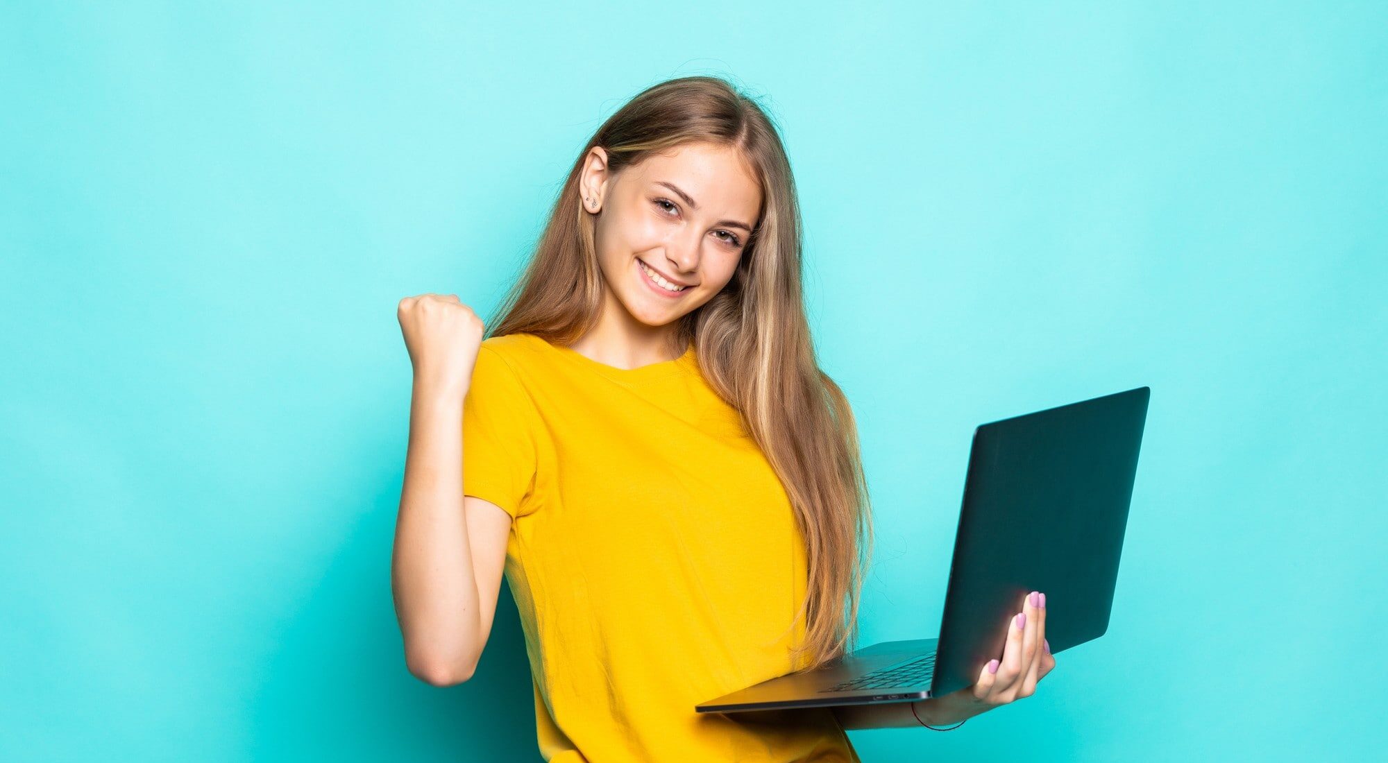 Eine junge Frau mit Laptop in der Hand macht eine Siegerpose vor türkisem Hintergrund
