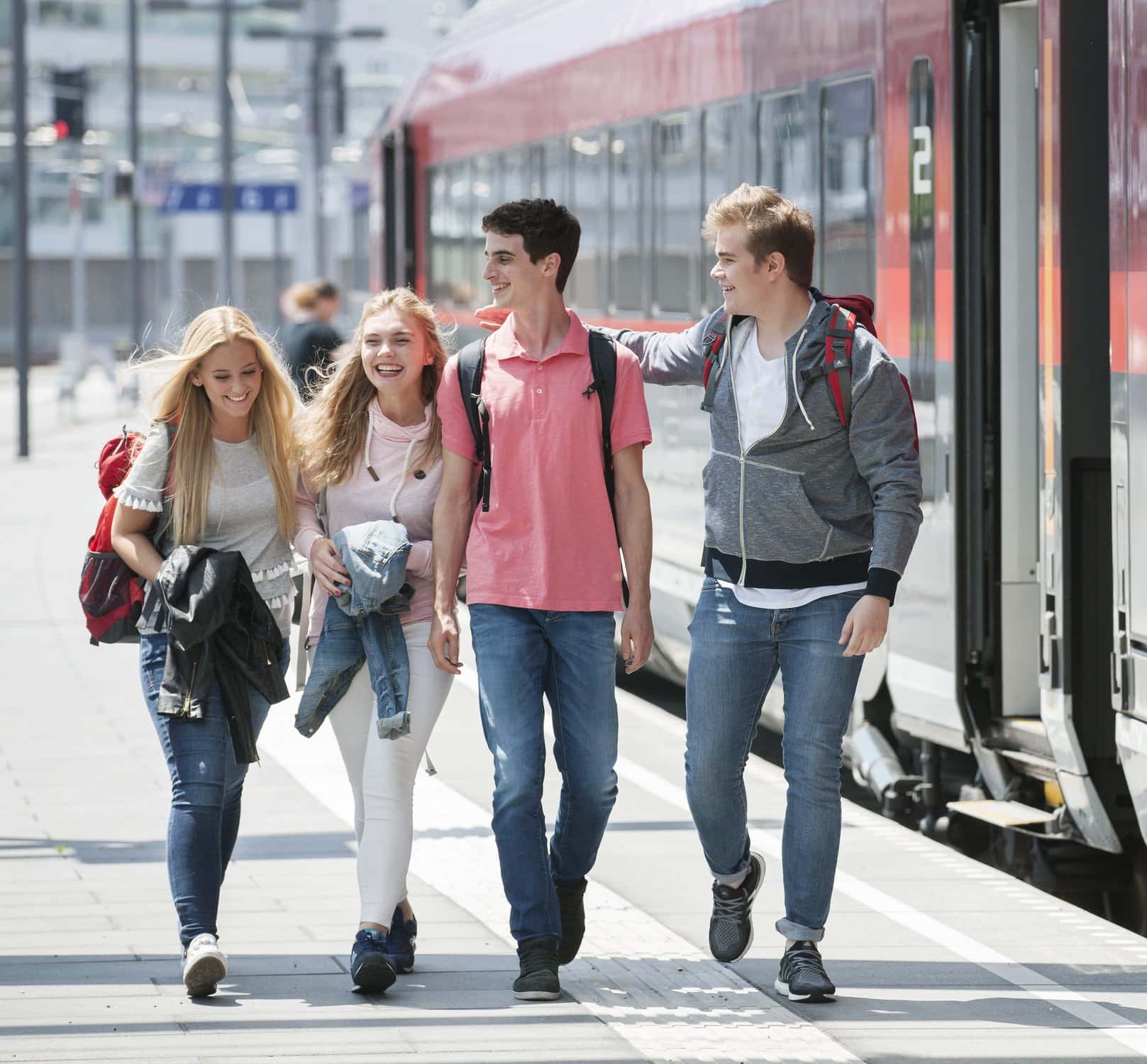 Vier Jugendliche gehen am Bahnsteig neben einem ÖBB-Zug entlang