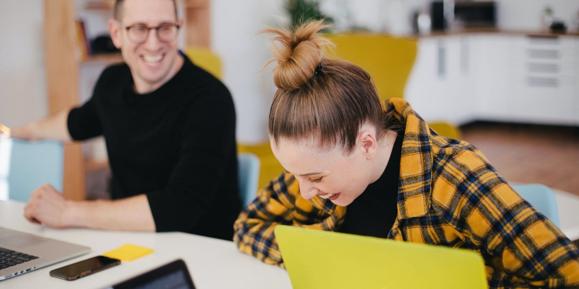 Junge Frau und junger Mann sitzen an Schreibtisch und lachen