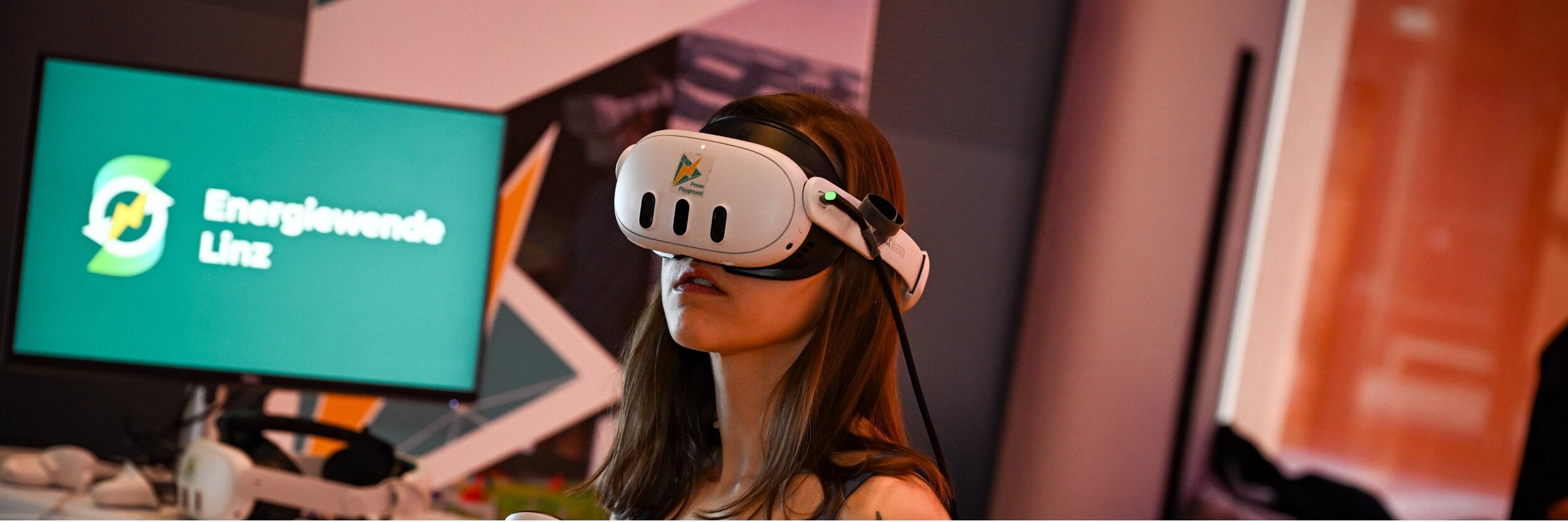 Junge Frau mit VR-Brille, im Hintergrund Schriftzug "Energiewende Linz" auf Bildschirm