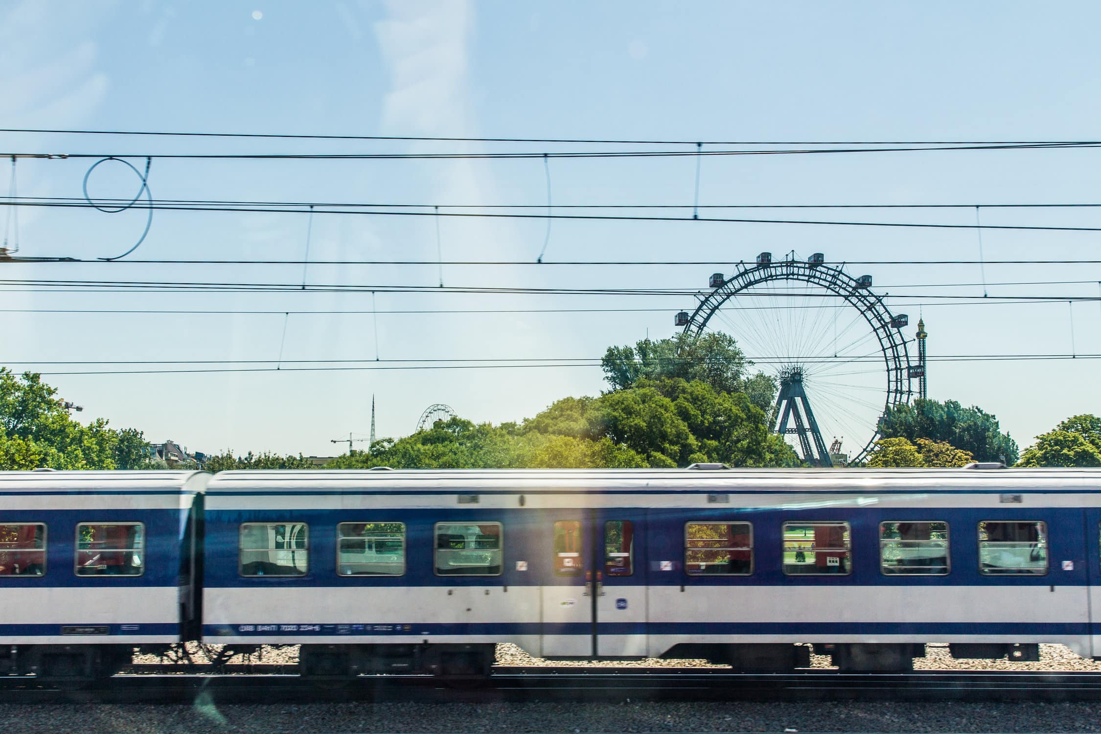 Blau/weißer Eisenbahnwaggon vor Bäumen und einem Riesenrad