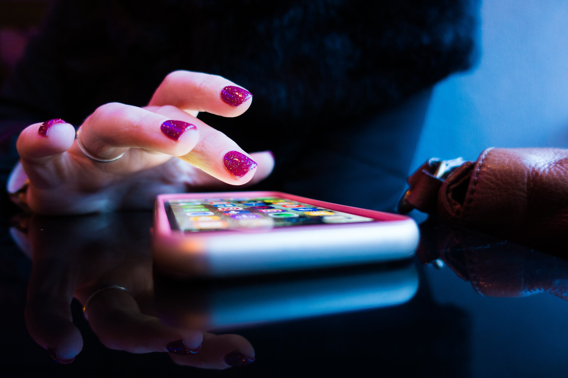 Hand mit lackierten Nägeln, die an einem Smartphone scrollt