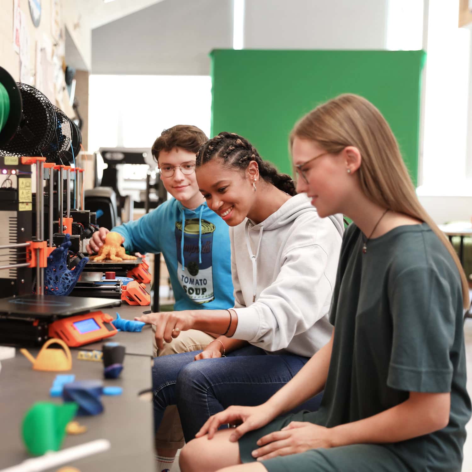 Drei Jugendliche sitzem an einem mit 3D-Druckern ausgestatteten Tisch im techLAB