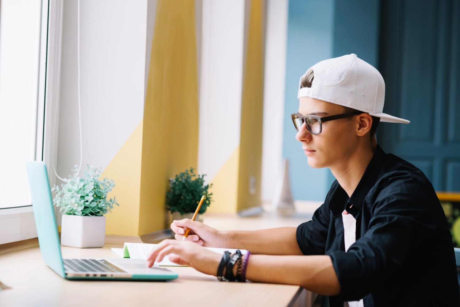 Junge sitzt mit Laptop vor Fenster